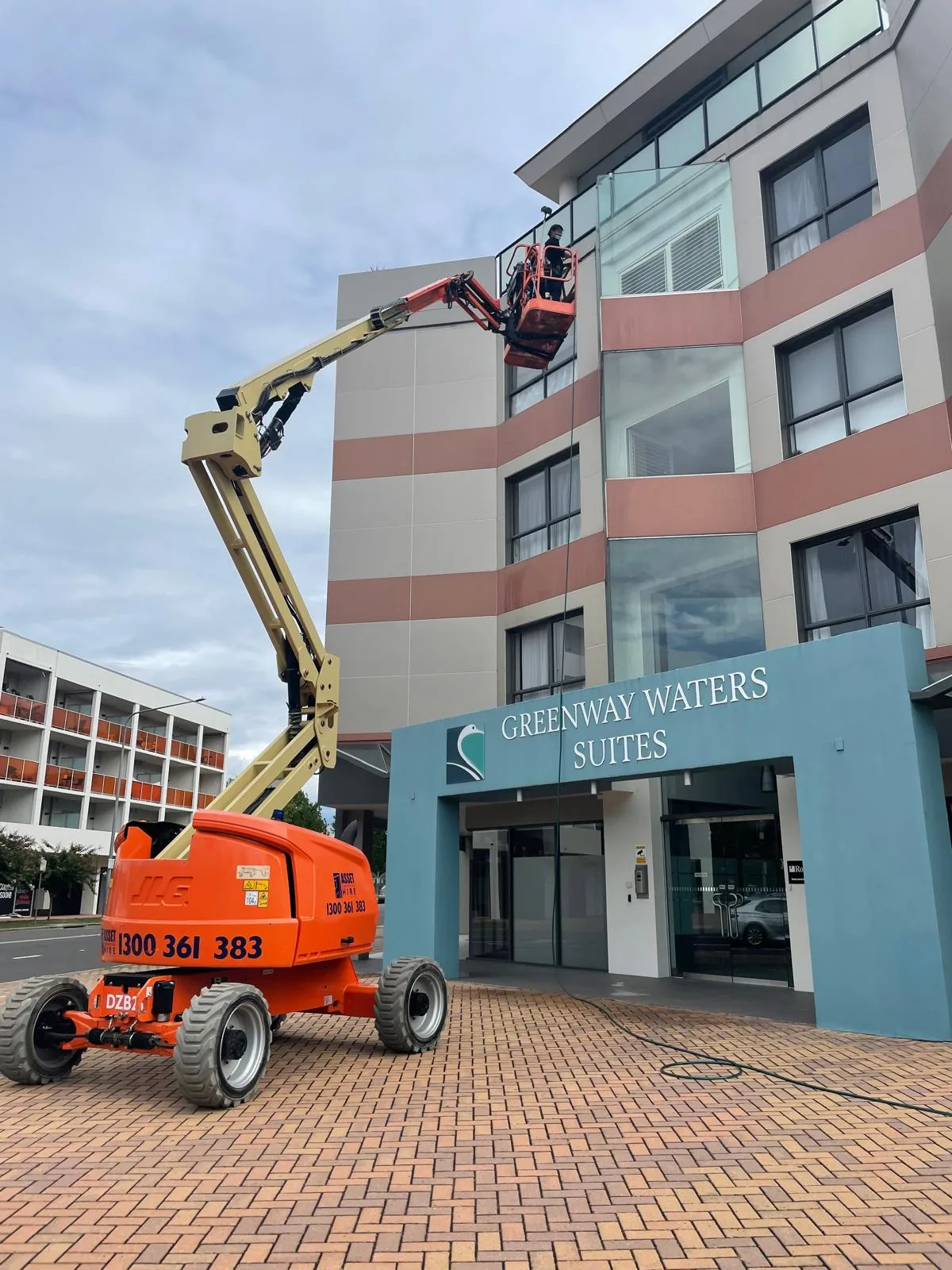 A worker in an orange boom-lift basket working the upper facade of an apartment building