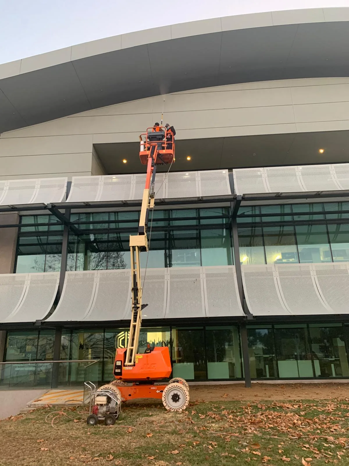 A boom lift extended at dusk against the curved metal fascia of a building