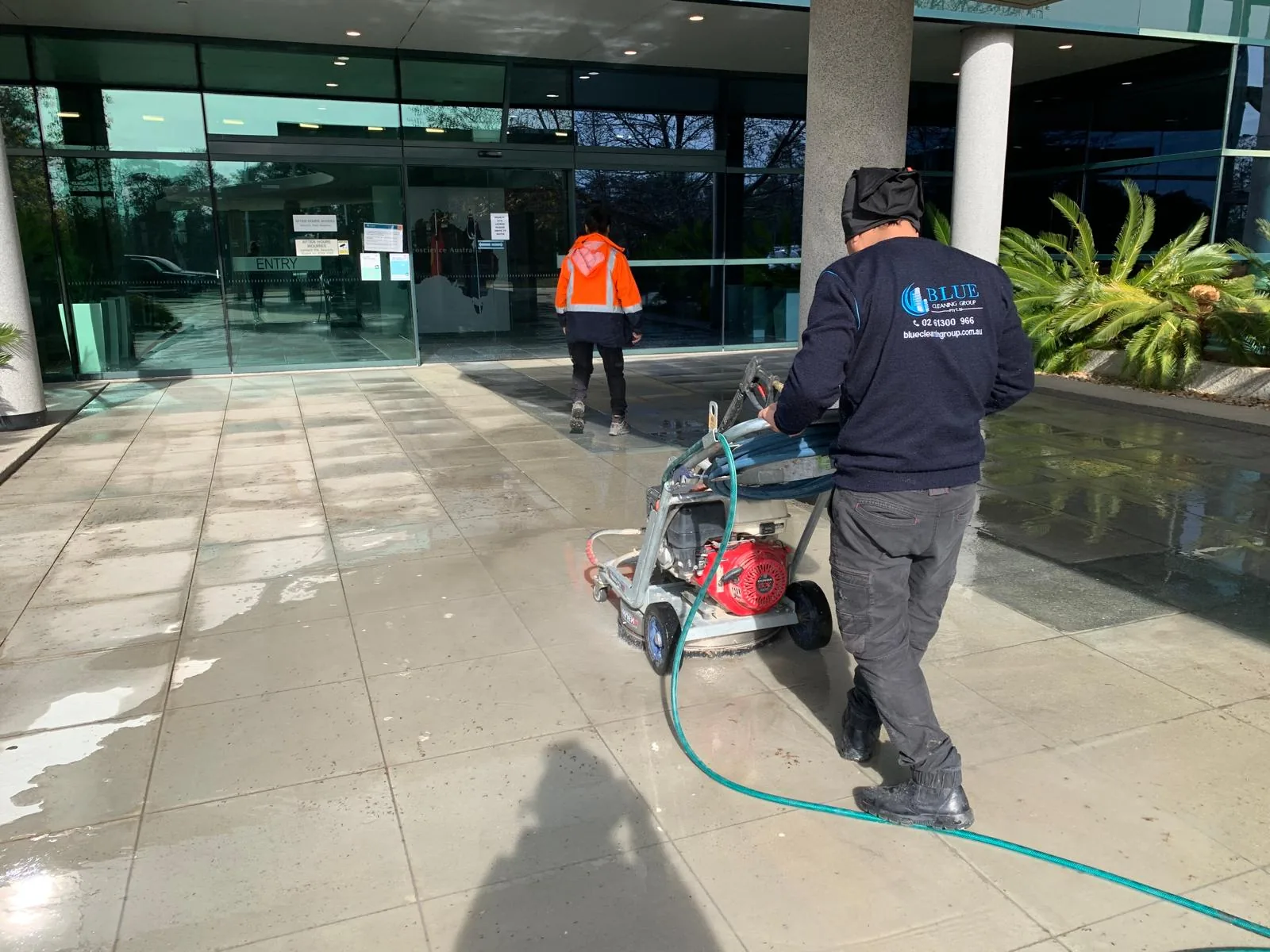 A Blue Cleaning Group worker driving a rotary surface cleaner across the forecourt of an office entrance