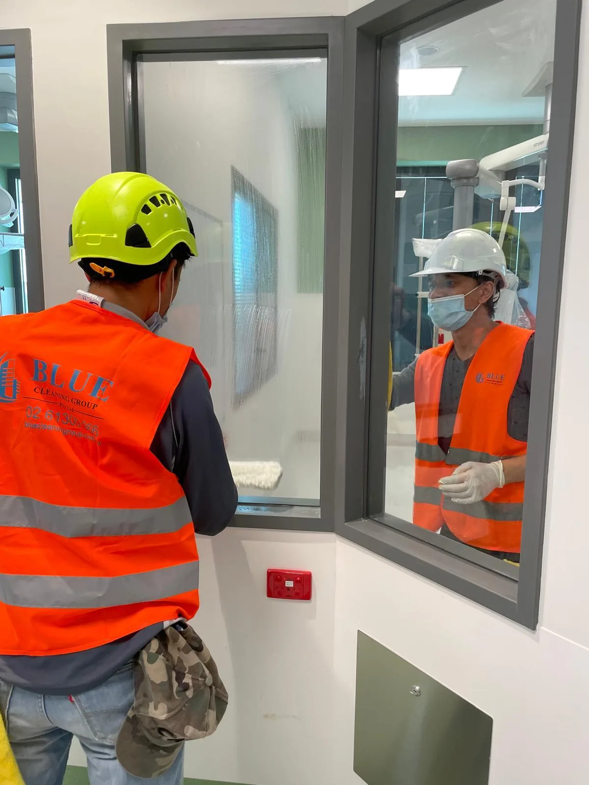 A cleaner in a Blue Cleaning Group vest wiping a full-height glass office partition