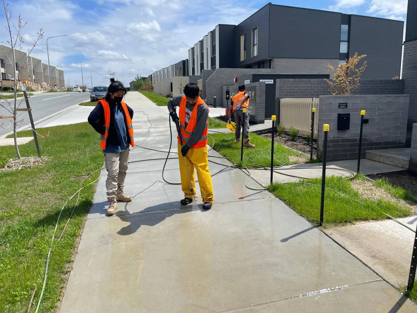 Three workers in hi-vis pressure washing the footpath outside a new townhouse