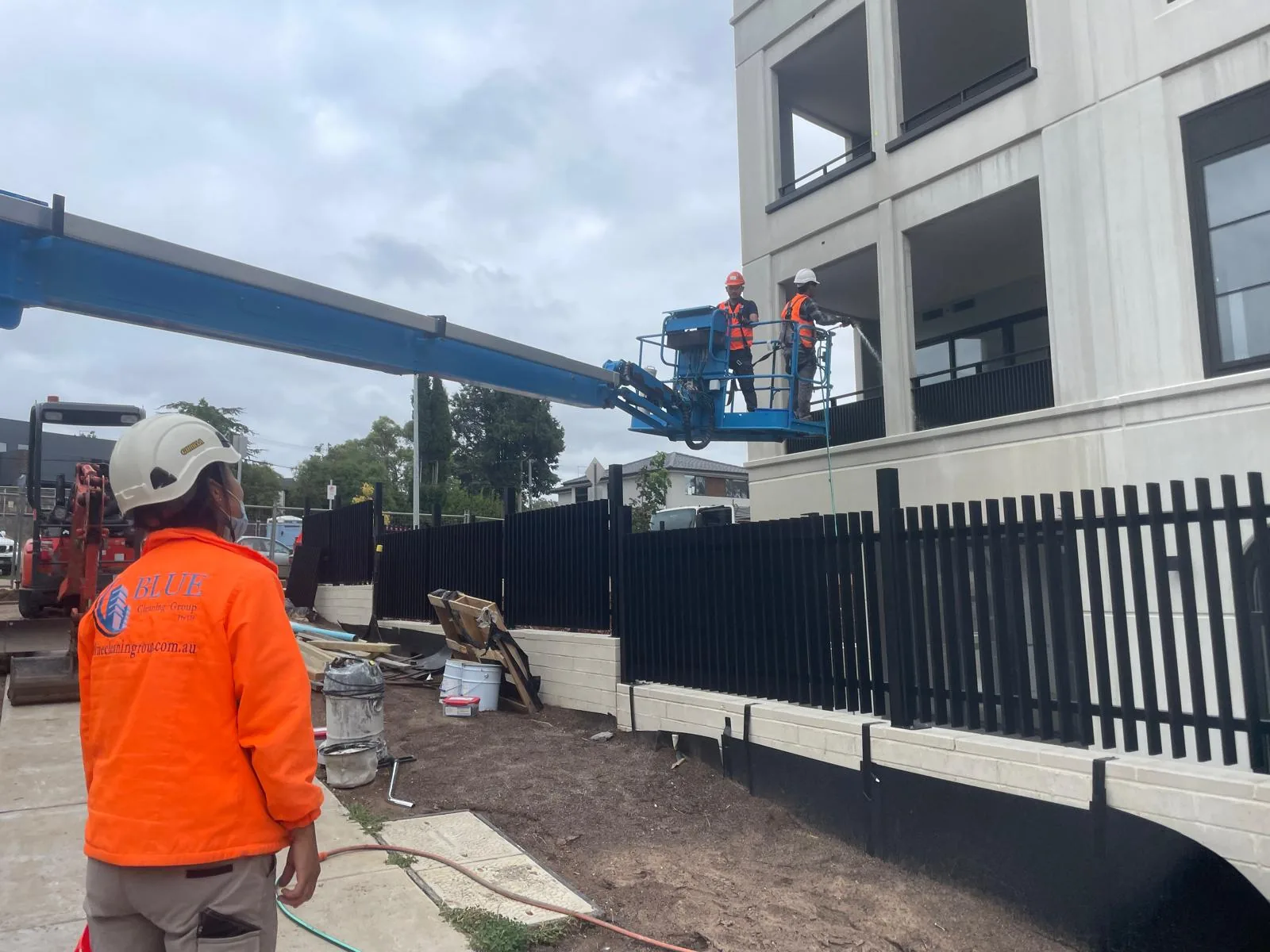 A Blue Cleaning Group spotter on the ground while two colleagues hose a new building's facade from a boom lift