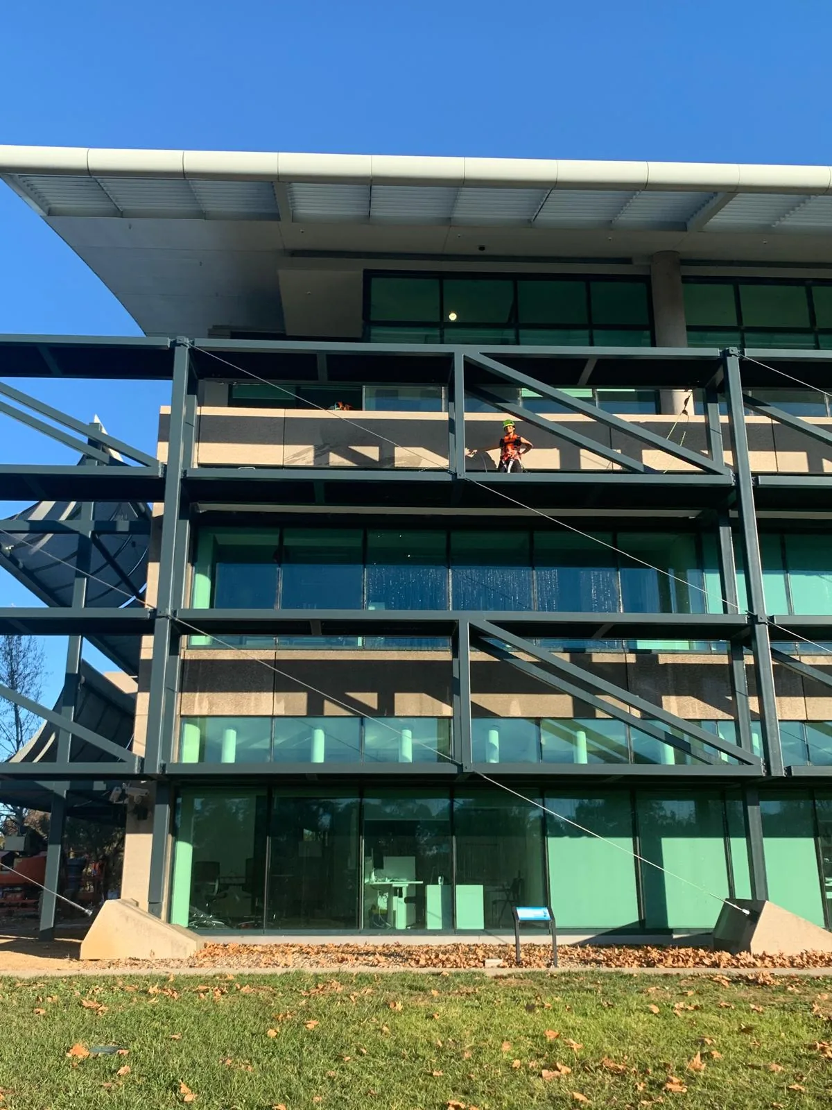 A worker in orange hi-vis and a harness standing two storeys up on the steel frame of a glazed facade