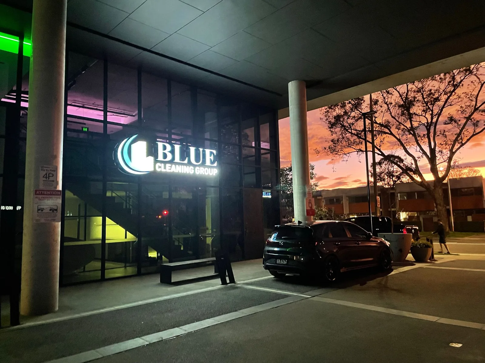 The Blue Cleaning Group office sign lit in the window of a glazed corner shopfront at dusk