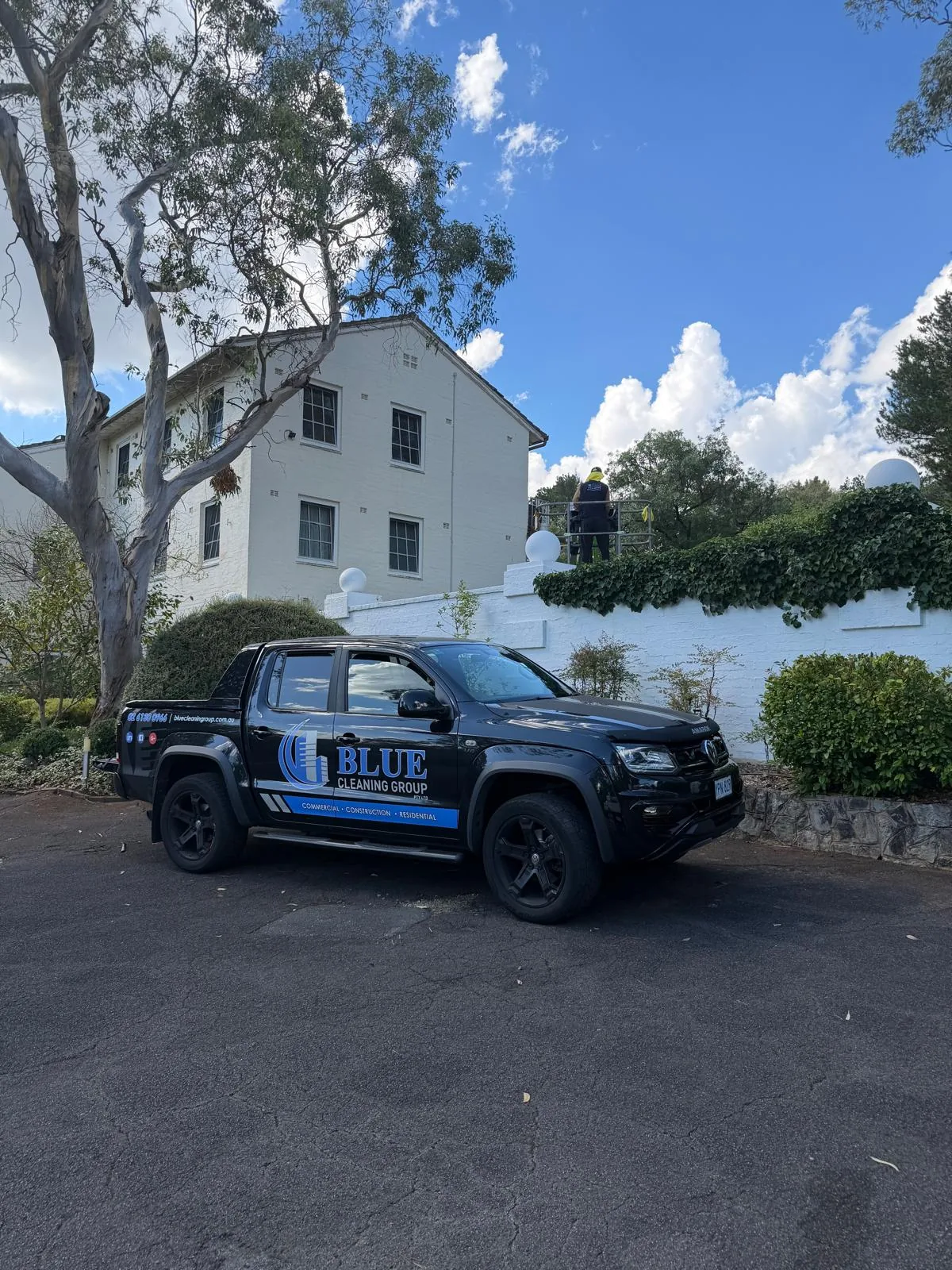 The signwritten Blue Cleaning Group dual-cab ute parked on a driveway below a two-storey rendered building