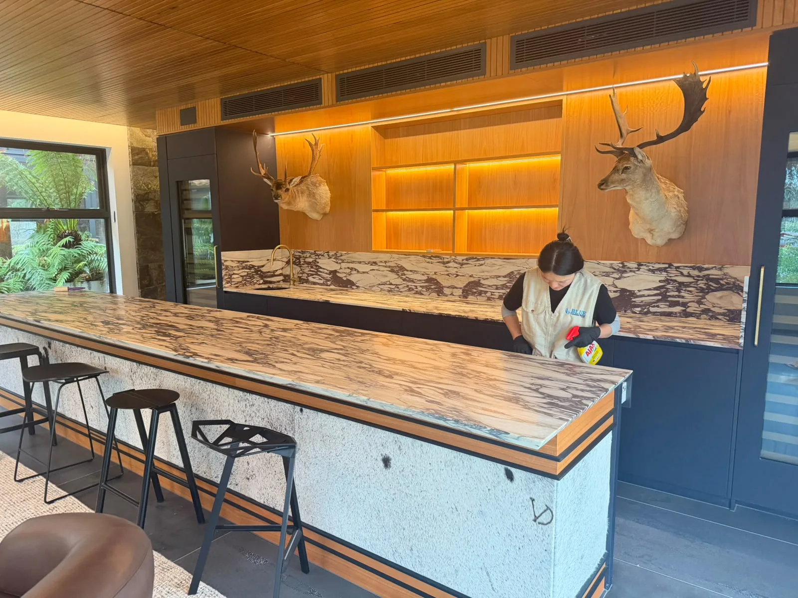 A private kitchen photographed from the doorway, a Blue Cleaning Group cleaner working at the marble island