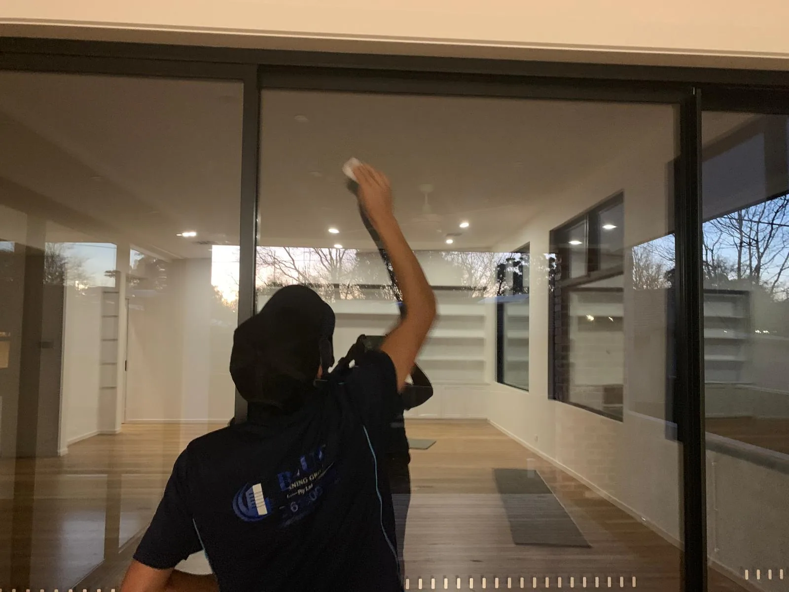 A Blue Cleaning Group cleaner wiping a full-height glass sliding door in an empty, newly finished house