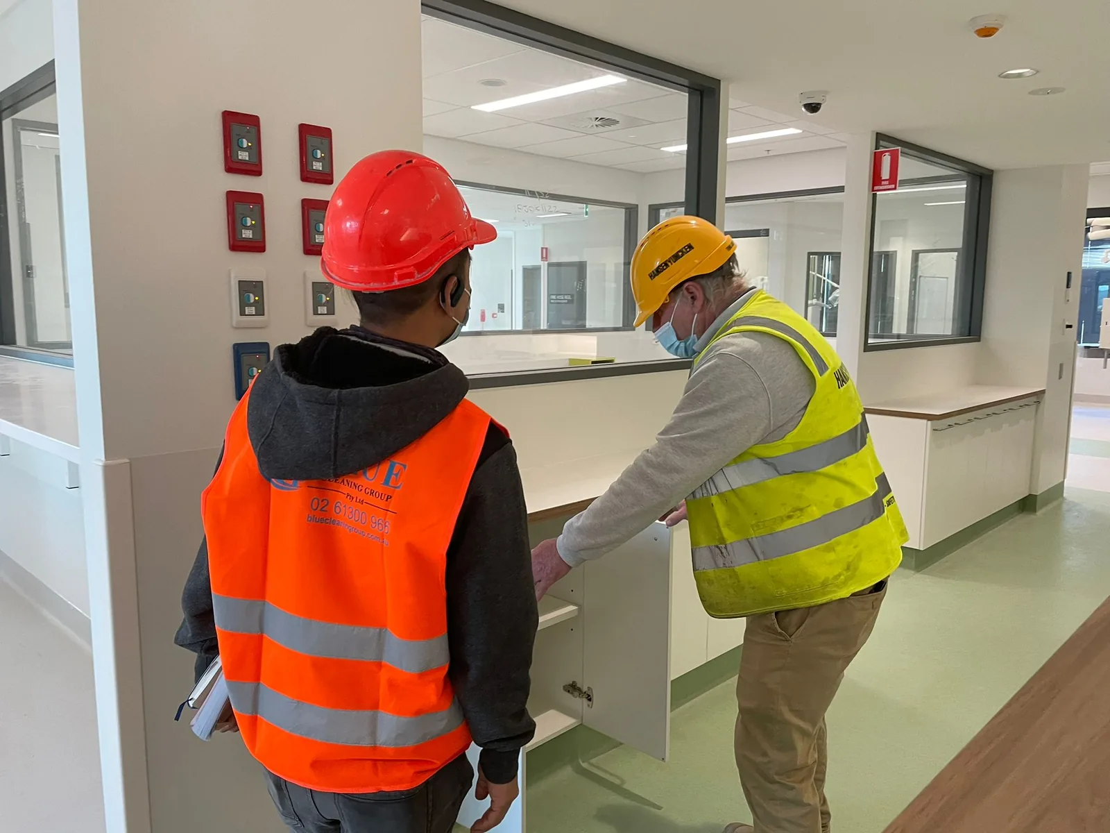 A Blue Cleaning worker and a builder in a hi-vis vest checking inside a joinery cabinet in a finished corridor