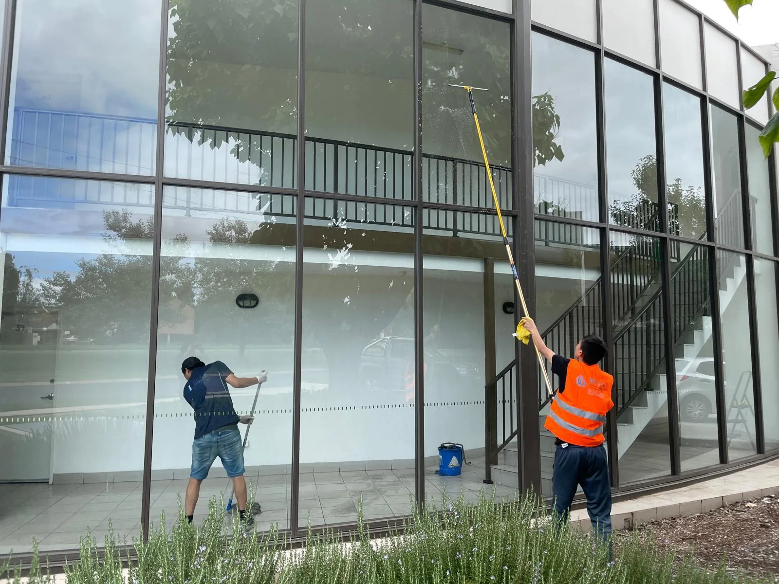 Two cleaners washing a curved glass curtain wall with a water-fed pole and a squeegee