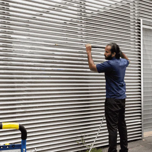 A worker pressure washing a louvred facade screen on a building exterior