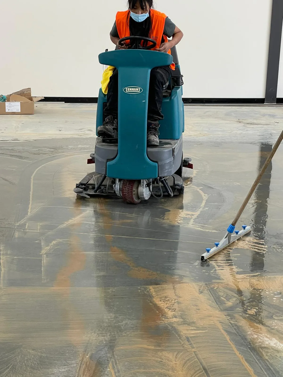 An operator on a Tennant ride-on scrubber lifting residue off a concrete slab