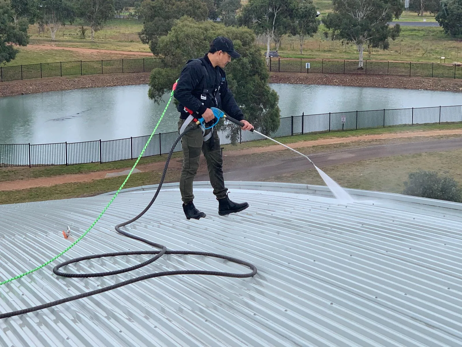 A worker on a harness walking a metal roof with a pressure lance
