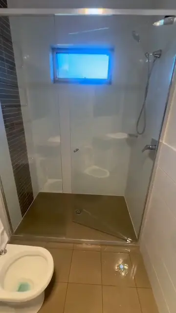 A finished glass shower recess in a home bathroom, screen clear and floor tiles washed