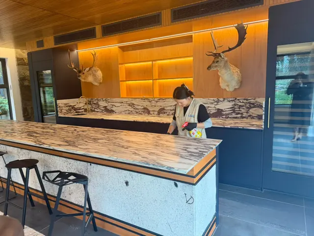 A cleaner in a Blue Cleaning Group tabard wiping the marble island bench of a private home's kitchen