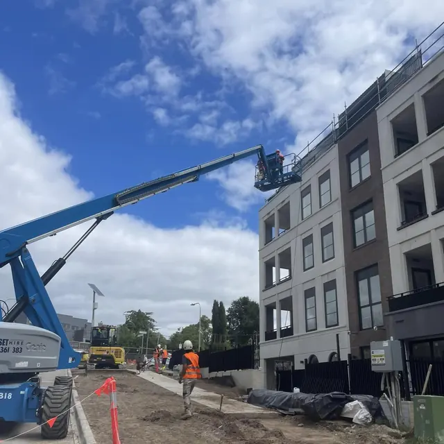 Two workers in a boom lift basket working at the roofline of an apartment block