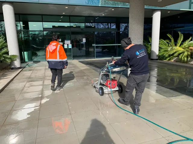 Two workers on the paved forecourt of a glazed office entrance