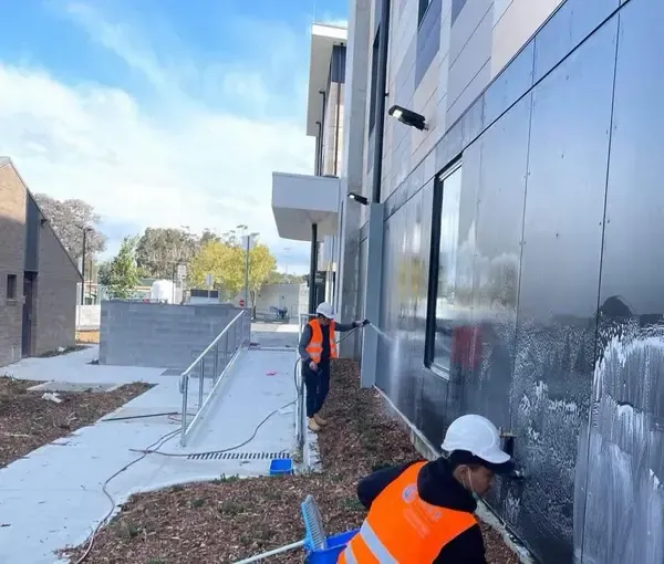 A crew pressure washing charcoal cladding panels on a building exterior
