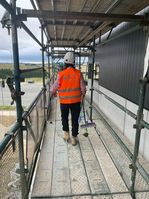 A worker in hi-vis on a scaffold walkway working on cladding panels