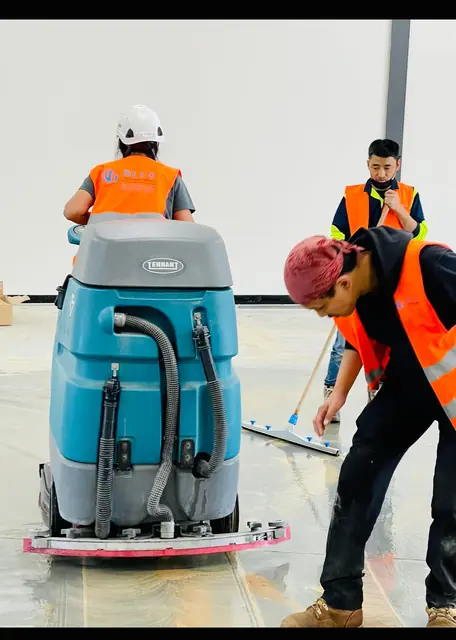Three cleaners working a flooded concrete floor with a Tennant walk-behind scrubber and a squeegee